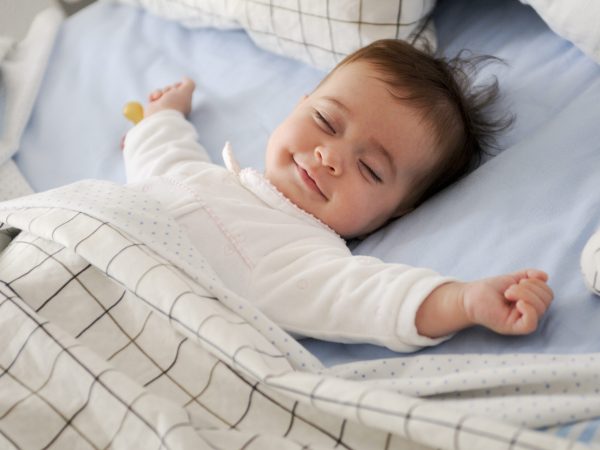 Smiling baby girl lying on a bed sleeping on blue sheets